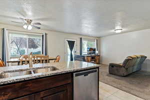 Kitchen featuring dark brown cabinetry, a textured ceiling, dishwasher, light carpet, and light stone countertops