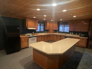 Kitchen with light countertops, freestanding refrigerator, white range with electric stovetop, brown cabinetry, and wooden ceiling