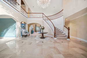 Entrance foyer featuring a towering ceiling, crown molding, a chandelier, arched walkways, and stairway