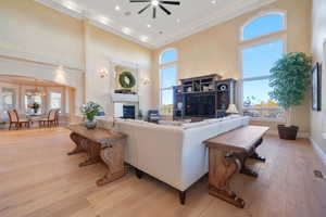 Living room with a high ceiling, a glass covered fireplace, crown molding, light wood-type flooring, and a chandelier