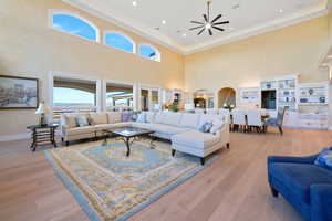 Living room with a towering ceiling, light wood-style floors, ornamental molding, arched walkways, and recessed lighting
