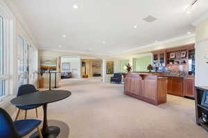 Living room with arched walkways, light colored carpet, crown molding, recessed lighting, and wet bar
