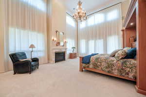 Carpeted bedroom with a high ceiling, a glass covered fireplace, a chandelier, and crown molding