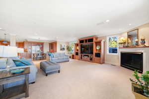 Living room with crown molding, a glass covered fireplace, plenty of natural light, recessed lighting, and light carpet