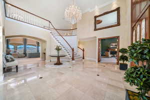 Foyer featuring arched walkways, a towering ceiling, crown molding, plenty of natural light, and a chandelier