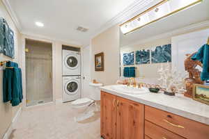 Bathroom featuring crown molding, a stall shower, vanity, stacked washing machine and dryer, and light tile patterned floors