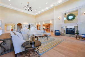 Living room featuring arched walkways, ceiling fan, ornamental molding, a high end fireplace, and a towering ceiling