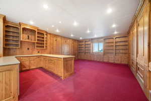 Kitchen featuring a peninsula, open shelves, wooden walls, light countertops, and dark colored carpet