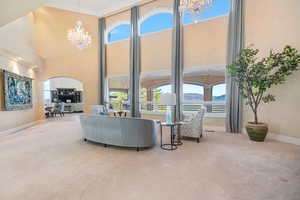 Living room with a chandelier, light colored carpet, crown molding, arched walkways, and a high ceiling