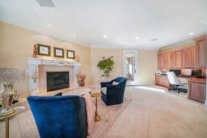 Living room featuring built in desk, crown molding, recessed lighting, a fireplace, and light colored carpet
