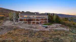 Back of property at dusk with a chimney, a mountain view, and a balcony