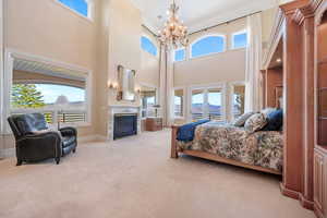 Bedroom featuring light colored carpet, a glass covered fireplace, crown molding, a high ceiling, and a chandelier