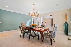 Dining area featuring stairs, a chandelier, ornamental molding, arched walkways, and light colored carpet