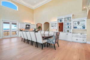 Dining room with crown molding, a towering ceiling, plenty of natural light, light wood-style floors, and arched walkways