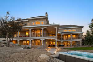 Rear view of house with a balcony, a patio area, a chimney, a hot tub, and stucco siding