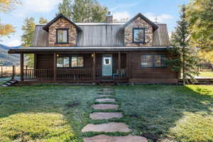 View of front of home featuring a metal roof, a front lawn, a chimney, and covered porch