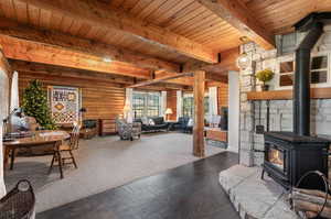 Living area featuring a wood stove, a wood ceiling with exposed beams, log walls, and dark stone finish flooring