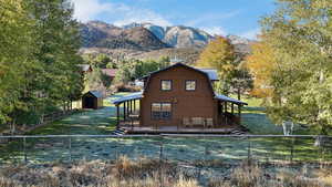Rear view of property with a gambrel roof, a fenced backyard, a storage unit, a deck with mountain view, and a chimney