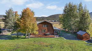 View of front of property featuring a gambrel roof, a deck with mountain view, a front yard, and an outdoor structure