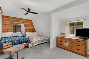 Bedroom with light colored carpet, multiple windows, ceiling fan, and rustic walls