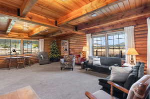 Carpeted living area with rustic walls and a wood ceiling with exposed beams