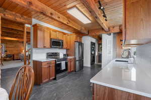 Kitchen featuring appliances with stainless steel finishes, a wood ceiling with exposed beams, tasteful backsplash, light stone countertops, and brown cabinets