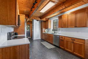 Kitchen featuring brown cabinetry, decorative backsplash, stainless steel appliances, a wooden ceiling with exposed beams, and rail lighting