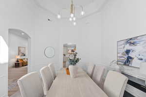 Dining area with a high ceiling, arched walkways, wood finished floors, a chandelier, and ornamental molding
