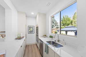 Kitchen with light wood-style floors, light stone counters, appliances with stainless steel finishes, white cabinets, and recessed lighting