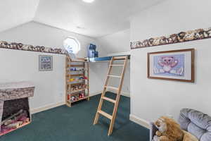 Carpeted bedroom featuring vaulted ceiling, a textured ceiling, and a fireplace