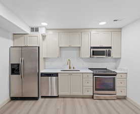 Kitchen featuring appliances with stainless steel finishes, recessed lighting, light wood-style flooring, and light stone counters