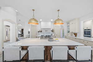 Kitchen featuring arched walkways, glass insert cabinets, a large island, decorative light fixtures, and a kitchen breakfast bar