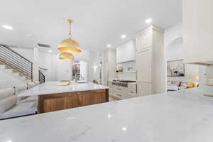 Kitchen featuring arched walkways, light stone counters, white cabinetry, pendant lighting, and a kitchen island with sink