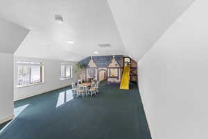 Rec room featuring a textured ceiling, vaulted ceiling, and carpet floors