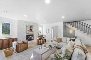 Living area featuring light wood-style floors, arched walkways, a stone fireplace, recessed lighting, and stairway