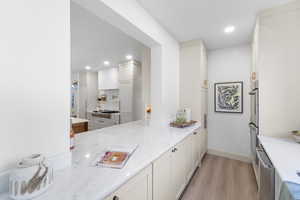 Kitchen with light wood-style floors, light stone counters, recessed lighting, appliances with stainless steel finishes, and a peninsula