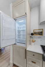 Kitchen with light stone countertops, light wood-style floors, paneled built in fridge, and stainless steel range with gas cooktop