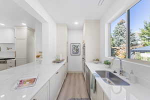 Kitchen with light stone countertops, light wood finished floors, stainless steel appliances, white cabinets, and recessed lighting