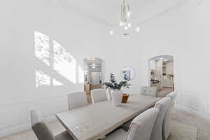 Dining area with a decorative wall, light carpet, a wainscoted wall, crown molding, and arched walkways