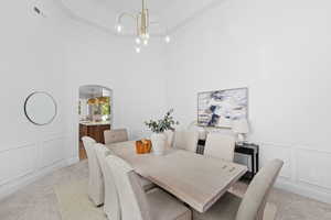 Dining room featuring a decorative wall, light carpet, a wainscoted wall, a towering ceiling, and arched walkways