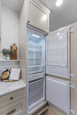 Kitchen view of fridge, white cabinets, and light stone countertops