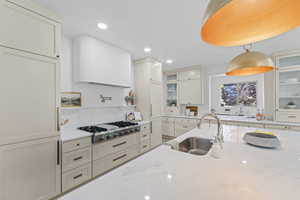 Kitchen featuring glass insert cabinets, light stone counters, decorative light fixtures, stainless steel gas stovetop, and recessed lighting