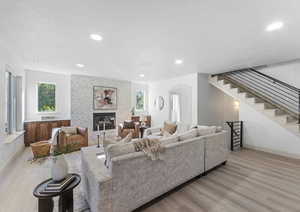 Living room featuring a fireplace, stairway, recessed lighting, light wood-style floors, and arched walkways