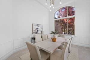 Dining area featuring a decorative wall, light colored carpet, a chandelier, a high ceiling, and wainscoting