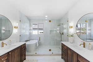 Full bathroom with two vanities, a freestanding bath, a shower stall, and light marble finish flooring