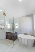 Full bathroom featuring vanity, marble finish flooring, tile walls, and a freestanding tub