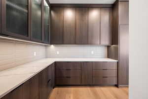 Kitchen with light wood-style floors, modern cabinets, glass insert cabinets, dark brown cabinetry, and decorative backsplash