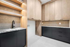 Kitchen featuring modern cabinets, backsplash, light stone counters, and light brown cabinetry