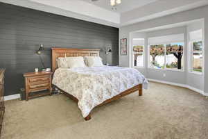 Bedroom featuring wood accent walls, bay window, carpet and ceiling fan.