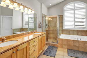 Bathroom featuring a garden tub, a walk-in shower, light tile patterned flooring, double vanity, and vaulted ceiling